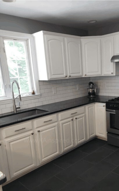 Same kitchen after renovation with white cabinets, dark counters and updated floor